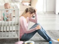 امرأة جالسة على الأرض وبجوارها طفلتها وتظهر عليها أعراض اكتئاب ما بعد الولادة.